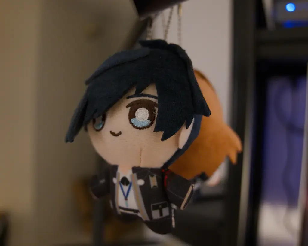 AI generated alt: A small plush figure of a dark-haired character hanging by a chain in a dim room, a blue indicator light behind it.